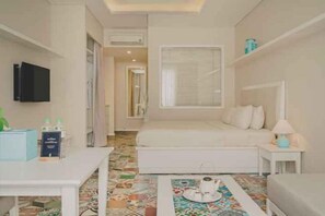 A small, well-lit room with a bed, a bedside table with a lamp, a TV mounted on the wall, and a colorful rug. - Yen Living Binh Th Nh (Ho Chi Minh Municipality)