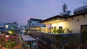 Una terraza en la azotea con una mesa y sillas, rodeada de plantas en macetas y un muro de piedra.