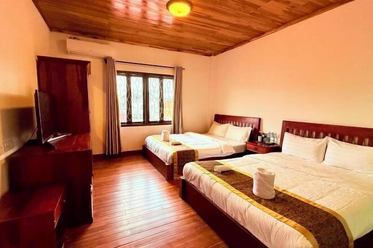 A hotel room with two beds, wooden flooring, a TV, and a window with curtains.