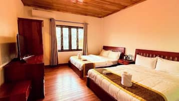 Habitación de hotel con dos camas, suelo de madera, televisor y ventana con cortinas.