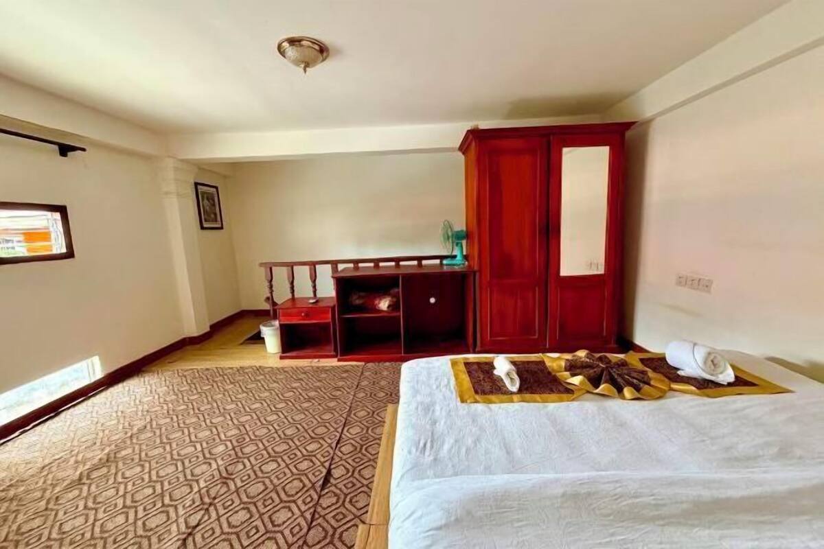 A hotel room with a bed, a wardrobe, a desk, and a patterned carpet.