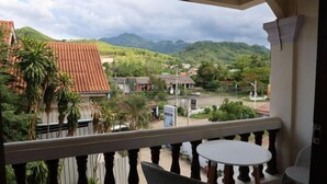 Un balcon avec une table et des chaises, d’où l’on peut admirer une ville avec ses bâtiments et, au loin, des montagnes.