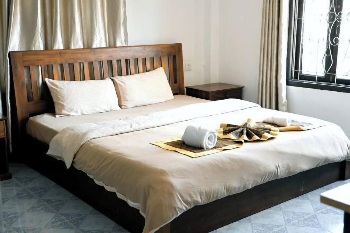 A neatly made bed with a wooden headboard, a small bedside table, and a window with curtains.