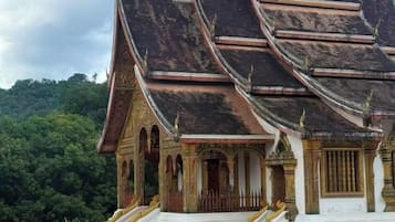 Un temple traditionnel à plusieurs niveaux, orné de décorations dorées et reposant sur une base blanche, qui se dresse sur une colline boisée.