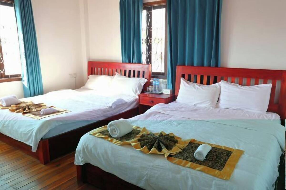 A hotel room with two beds, each with white linens and a red headboard. There are towels and a decorative item on the beds.
