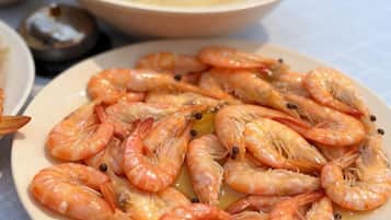 A plate of cooked shrimp with a sauce, accompanied by a bowl of soup and a small container of condiments.