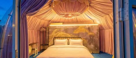 A luxurious, circular room with a bed centered in the middle, draped curtains, and a unique ceiling design.