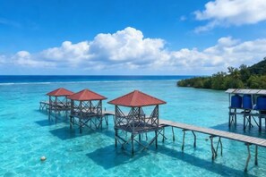 Overwater bungalows with wooden walkways and red roofs, connected by a wooden deck, overlooking clear turquoise water and a distant shoreline. - Turtle Garden Resort @ Semporna (Semporna)