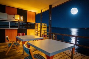 Un patio con tavoli e sedie, affacciato su uno specchio d'acqua con la luna nel cielo.