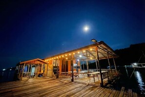 Un pontile in legno con posti a sedere all'aperto, una zona riparata con luci a tendina e vista sull'acqua.