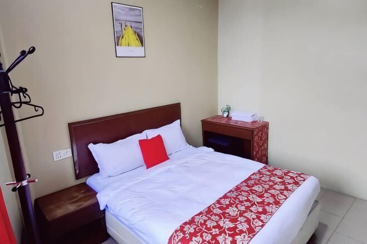 A neatly made bed with white and red bedding, a small bedside table with a lamp, and a wall-mounted picture.