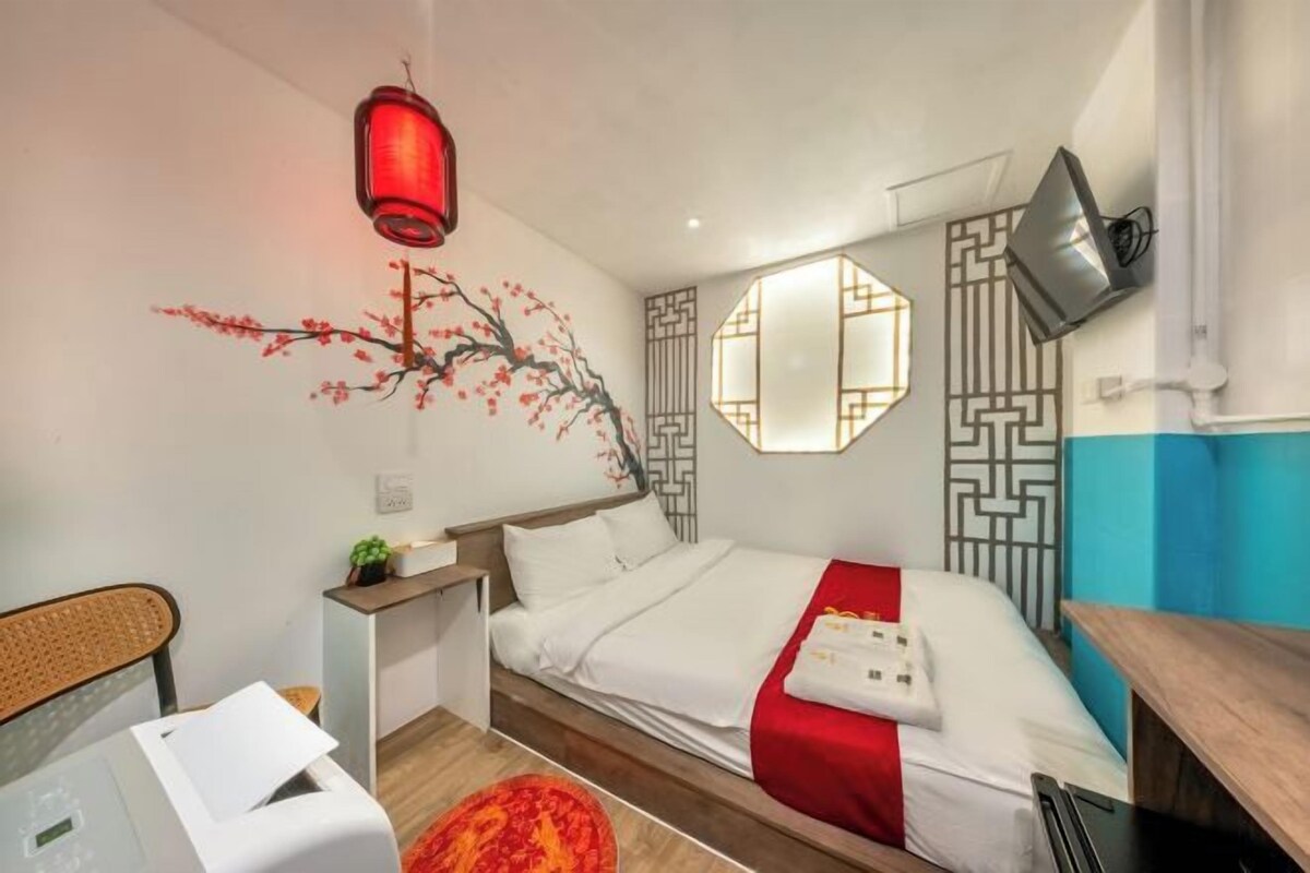 A hotel room with a bed, a desk, a chair, and a wall-mounted TV.
