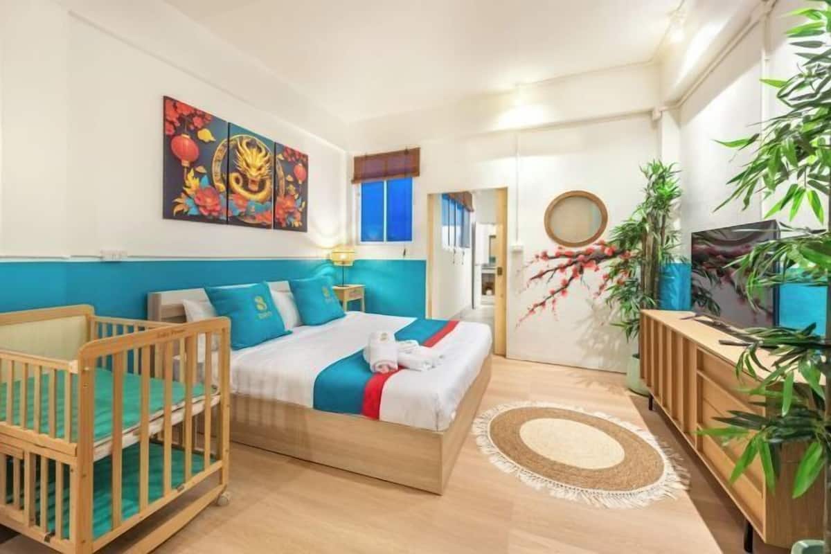 A modern bedroom with a wooden bed, a crib, a blue accent wall, and a large painting.
