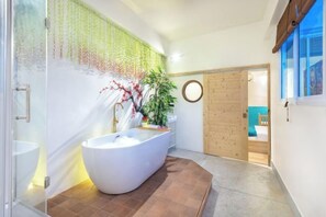 A modern bathroom with a freestanding bathtub, a glass shower enclosure, and a wooden door leading to a bedroom. - Shin Hotel Chinatown (Bangkok)