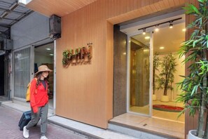 A hotel entrance with a wooden facade, a glass door, and a visible interior with plants. - Shin Hotel Chinatown (Bangkok)