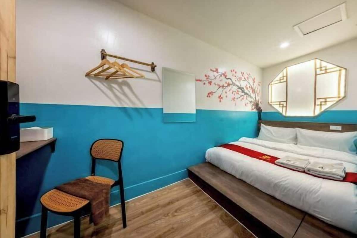 A hotel room with a bed, a chair, a wall-mounted towel rack, a mirror, and a decorative wall piece.