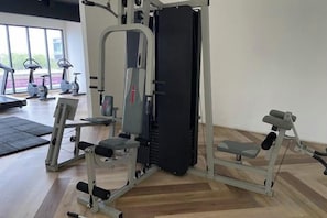 Een sportschool met trainingsapparatuur, een gewichtbank en een squatsysteem aan de muur.