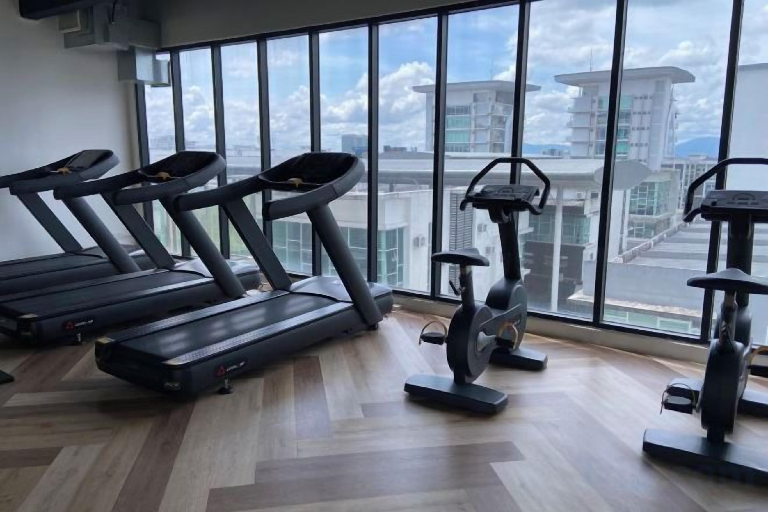 A gym with treadmills and an elliptical machine, large windows with a city view.