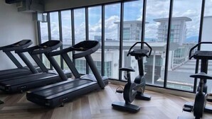 Une salle de sport équipée de tapis de course et d’un appareil elliptique, avec de grandes fenêtres offrant une vue sur la ville.