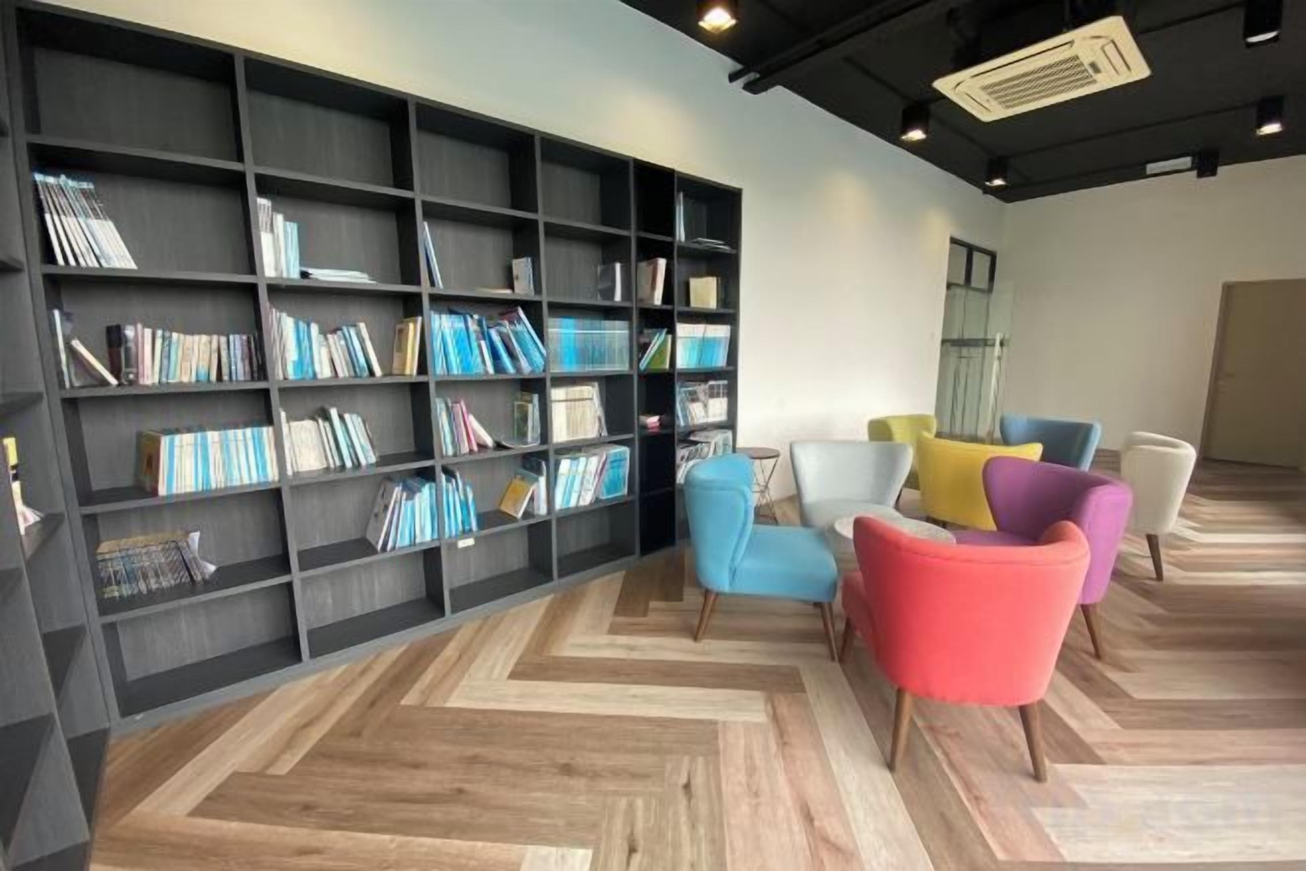 A modern interior with a large bookshelf, multiple colorful chairs, and a herringbone-patterned floor.
