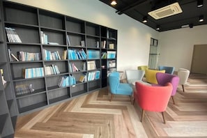 A modern interior with a large bookshelf, multiple colorful chairs, and a herringbone-patterned floor. - Gala Residences @ Galacity (Kuching)