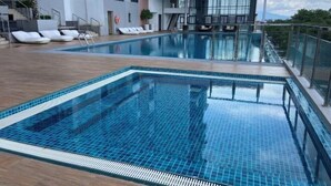 Une piscine extérieure moderne, avec une eau d’un bleu cristallin, entourée d’une terrasse en bois et de chaises longues blanches.
