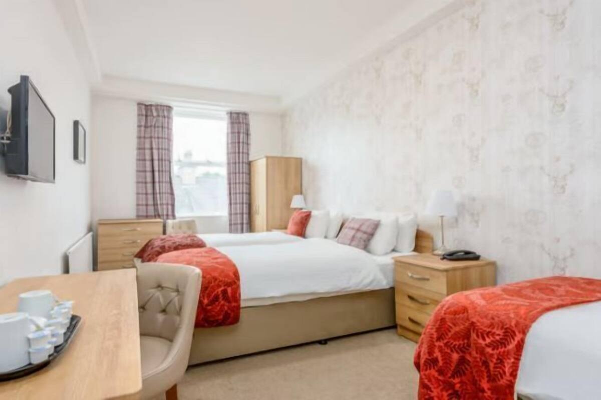 Une chambre d’hôtel avec deux lits, un bureau avec une chaise, une armoire et un téléviseur fixé au mur.
