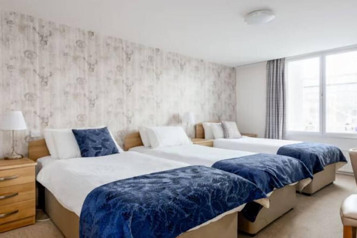 Une chambre d’hôtel avec deux lits, une table de chevet, une lampe et une grande fenêtre.