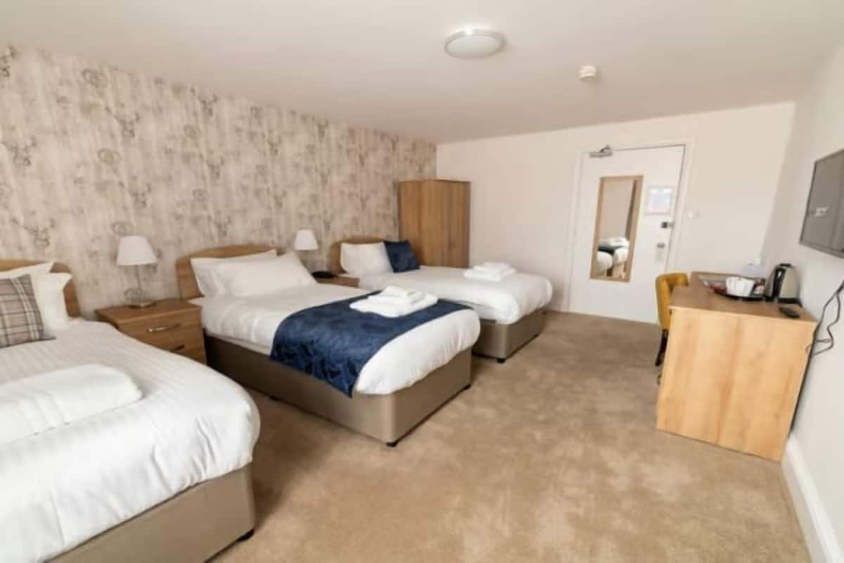 Une chambre d’hôtel avec deux lits, une armoire en bois, un bureau avec une chaise et un miroir au mur.