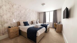 Une chambre d’hôtel avec deux lits, un bureau, une chaise, une lampe et un téléviseur à écran plat.