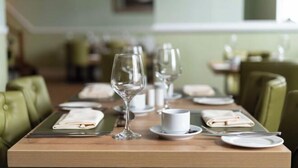 Une table à manger dressée avec des assiettes, des verres et des couverts, et des chaises recouvertes d’un tissu vert.