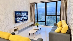 Un salon moderne doté d’un grand téléviseur, de sièges confortables, d’une petite table et offrant une vue sur la ville grâce à de grandes fenêtres.