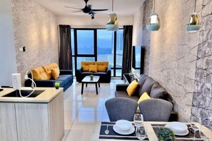 A modern hotel room with a dining area, a sofa, a coffee table, and a view of the city. - MidValley Southkey Mosaic 6-9pax Netflix-SmartTV70inch (Plentong)