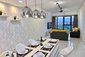 A modern living room with a dining area, a sofa, a TV, and a large window. - MidValley Southkey Mosaic 6-9pax Netflix-SmartTV70inch (Plentong)
