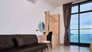 Une chambre moderne avec un canapé, une petite table, un miroir, une armoire et une grande fenêtre donnant sur la mer.