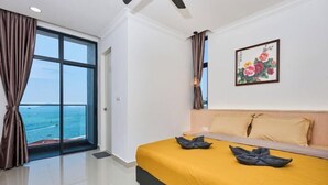 Une chambre d’hôtel avec une grande fenêtre, un lit recouvert d’une courtepointe jaune et un tableau accroché au mur.