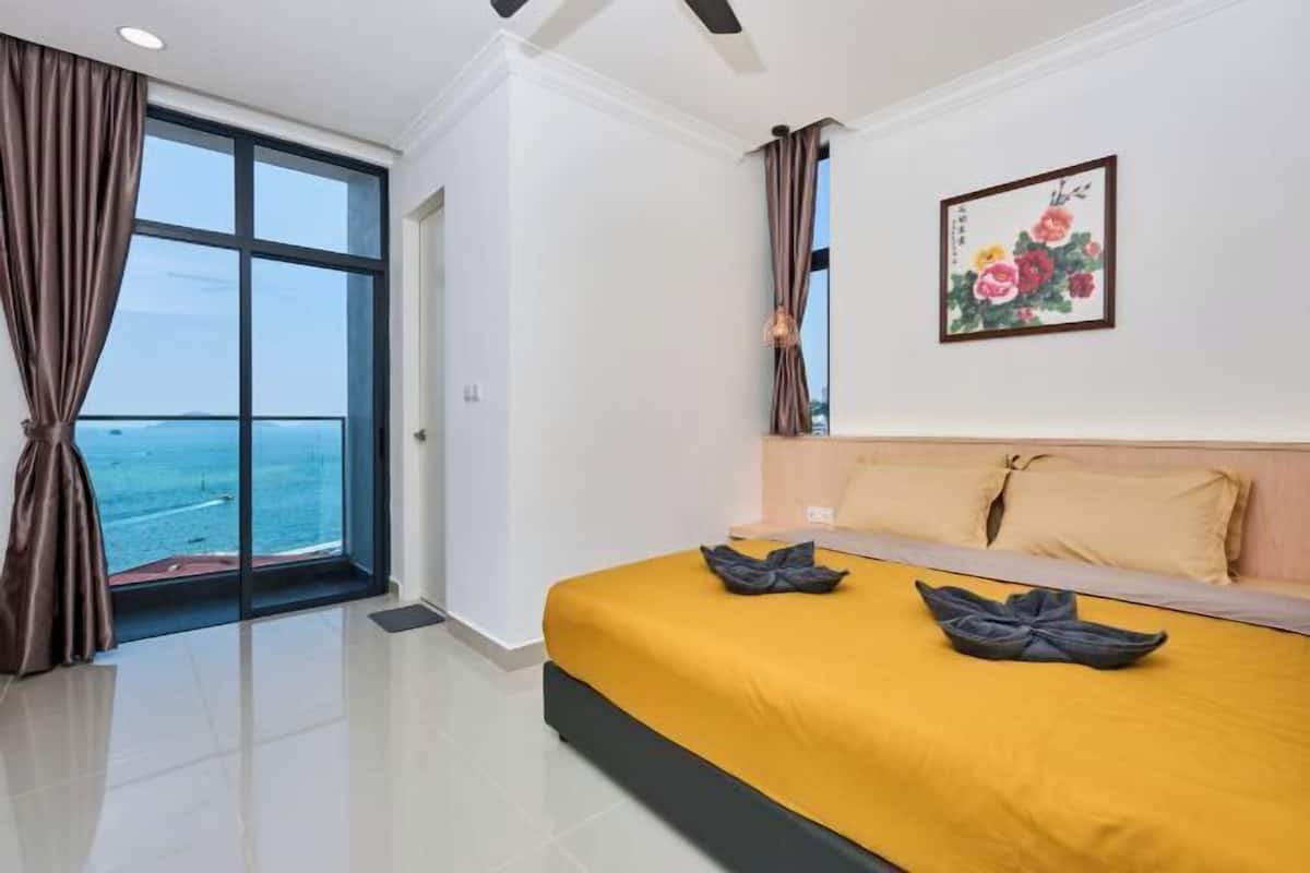 Una habitación de hotel con un ventanal grande, una cama con cubrecama amarillo y un cuadro en la pared.