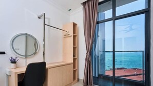 Une chambre équipée d’un bureau, d’une chaise, d’une armoire et d’une grande fenêtre donnant sur la mer.