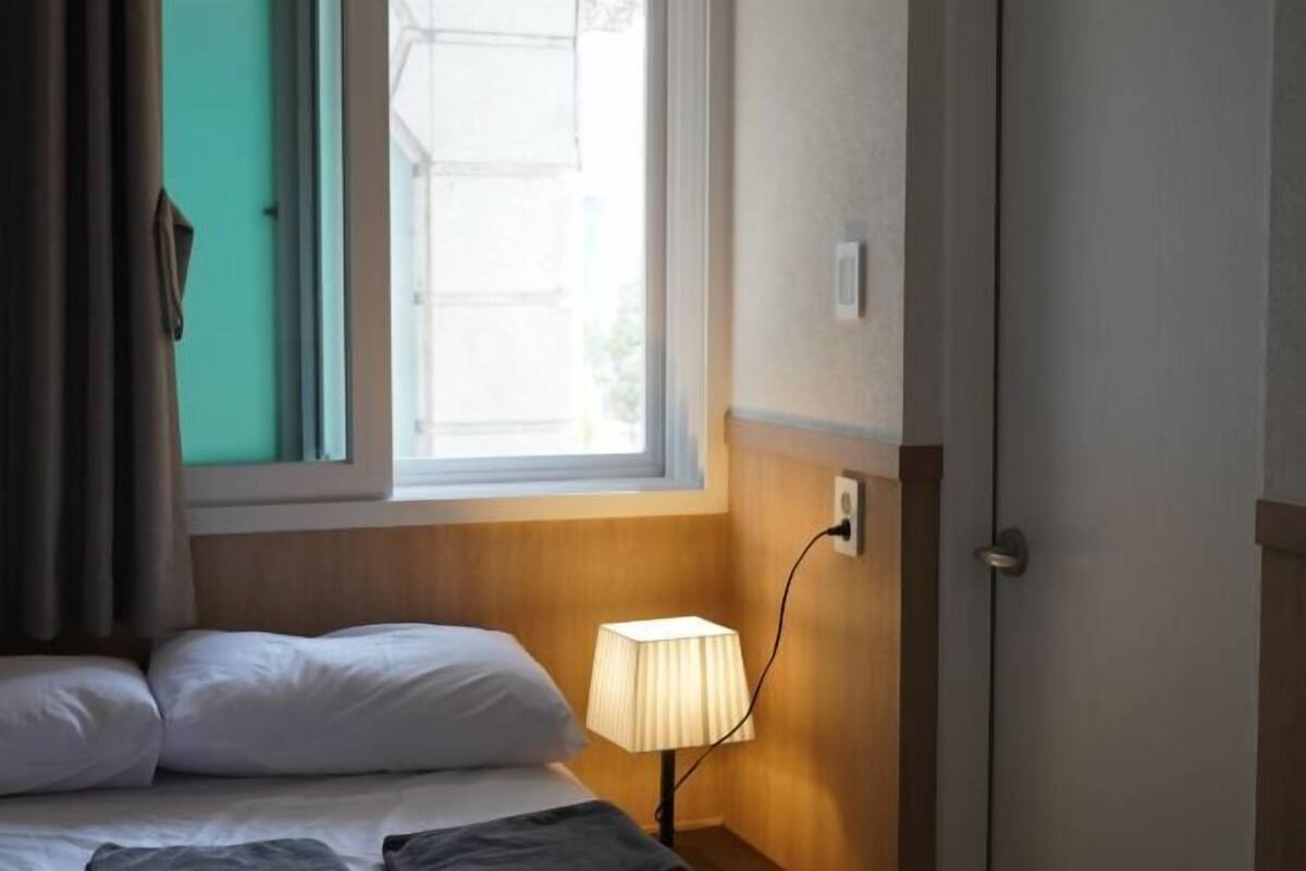 A hotel room with a bed, a bedside lamp, a window, and a door.