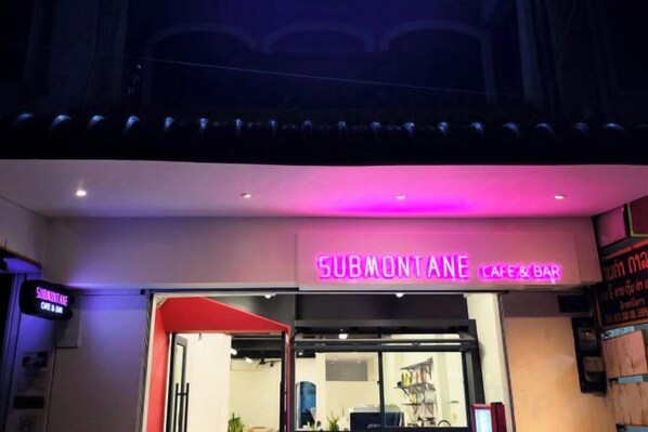 A Submontane cafe & bar with a neon sign, a glass door entrance, and a red awning. - Truman Hostel (Luang Prabang)