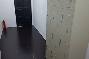 Un couloir avec un sol noir, un extincteur et une rangée de casiers beiges.