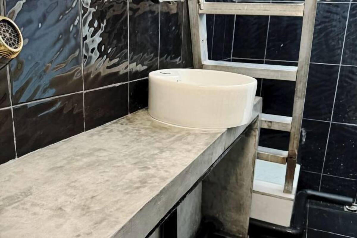 A bathroom with a white sink, black tiled walls, and a metal ladder.