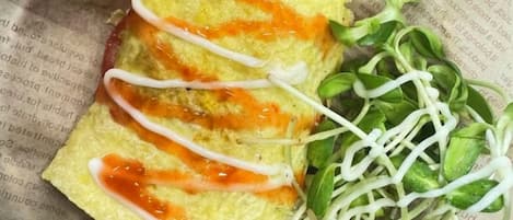 A folded omelette with sauce drizzled on top, accompanied by a side of sprouts.