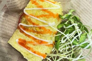 Une omelette pliée nappée de sauce, accompagnée d’une portion de jeunes pousses.