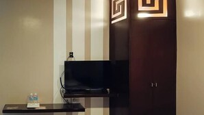Una habitación con una televisión de pantalla plana montada, una mesita con botellas de agua y un par de pantuflas.