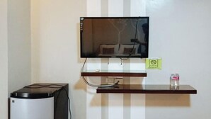 Un televisor montado en la pared con un decodificador y una botella de agua sobre un estante.