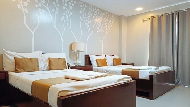 Habitación de hotel con dos camas, una mesita de noche, una lámpara y un muro con diseño de árbol.