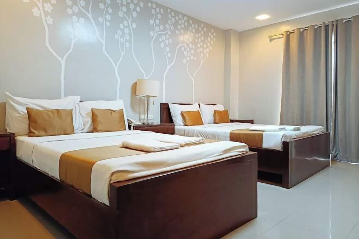 A hotel room with two beds, a nightstand, a lamp, and a wall with a tree design.