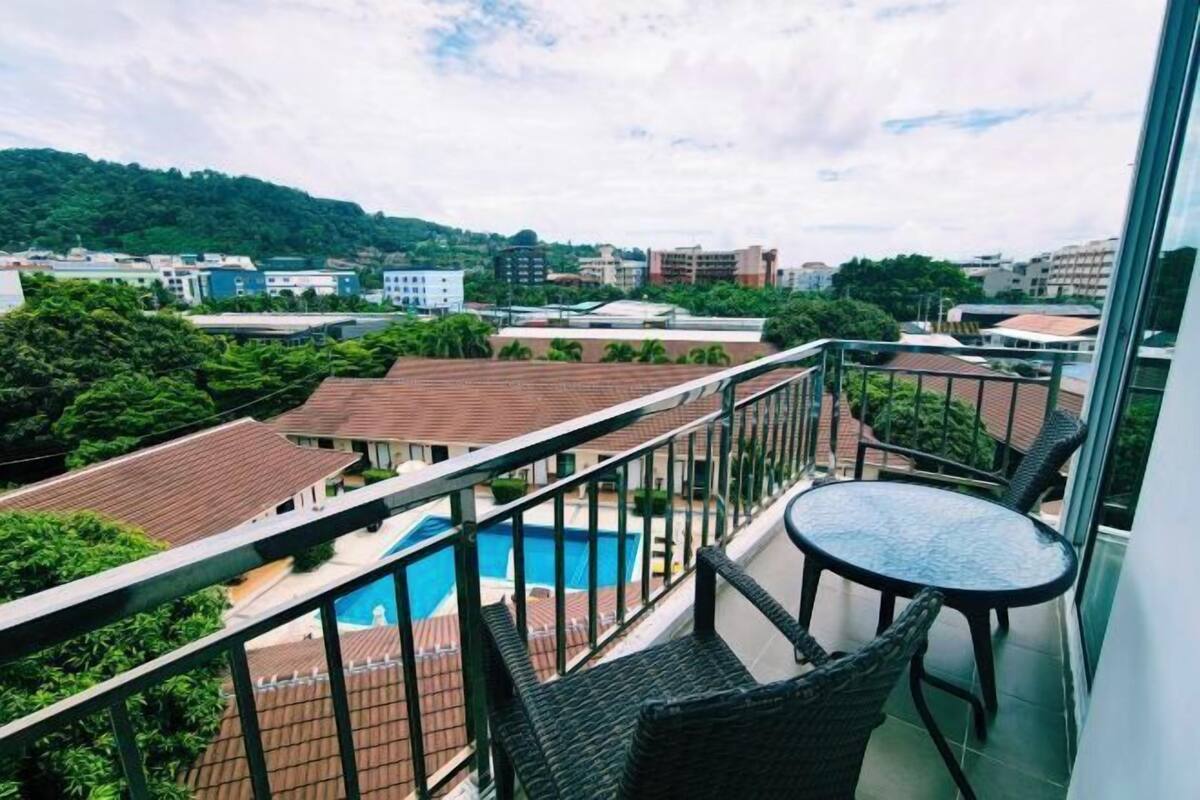 A balcony with wicker furniture, a view of a swimming pool, and surrounding buildings.