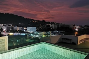 A rooftop pool with a tiled floor, surrounded by buildings and a sunset sky. - Forest Island Hotel (Phuket)